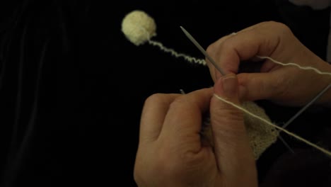 grandmother crafting socks with traditional spears, using natural sheep's wool, with a yarn skein as backdrop