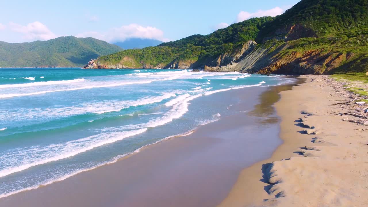 le onde colpiscono la sabbia bagnata riflettente su una spiaggia tropicale, un paesaggio di montagna verde soleggiato e un bellissimo mare blu