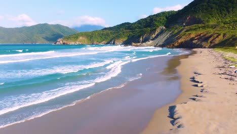 las olas golpean la arena húmeda reflectante en una playa tropical, un paisaje de montaña verde soleado y un hermoso mar azul