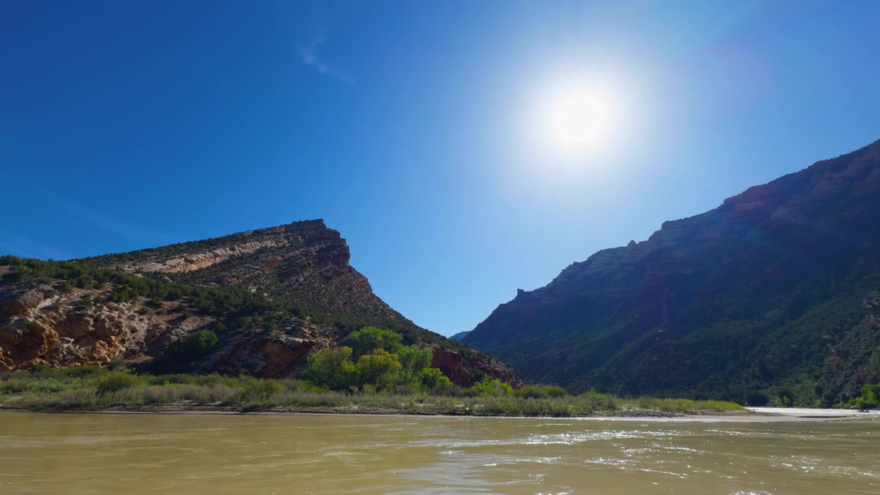 Uma mesa desértica iluminada pelo sol e paisagem fluvial sob céus claros no Colorado, estabelecendo um amplo cenário.