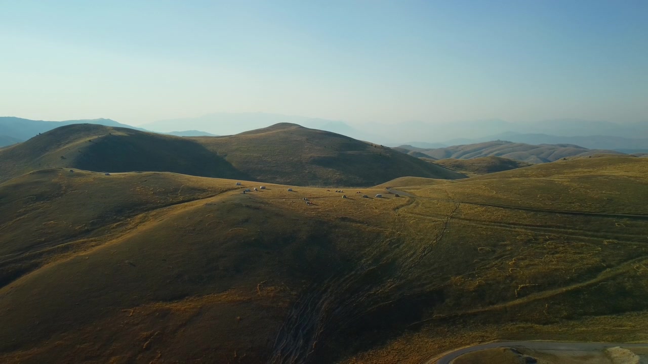 Alba su colline gialle e camper, ripresa aerea in discesa da drone. Vasto paesaggio sconfinato di prateria dorata e secca con camper accampati su una vetta.