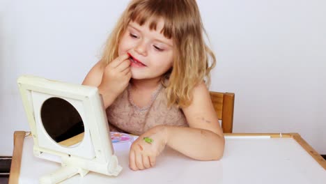 little girl plays with her make up, applying lipstick while watching herself in the mirror