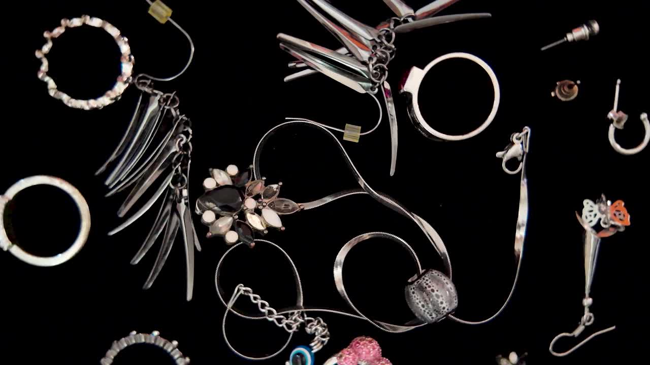 Assortment of stylish jewelry including necklaces, rings, bracelets and earrings, creating a glamorous display on a dark background. rotating shot