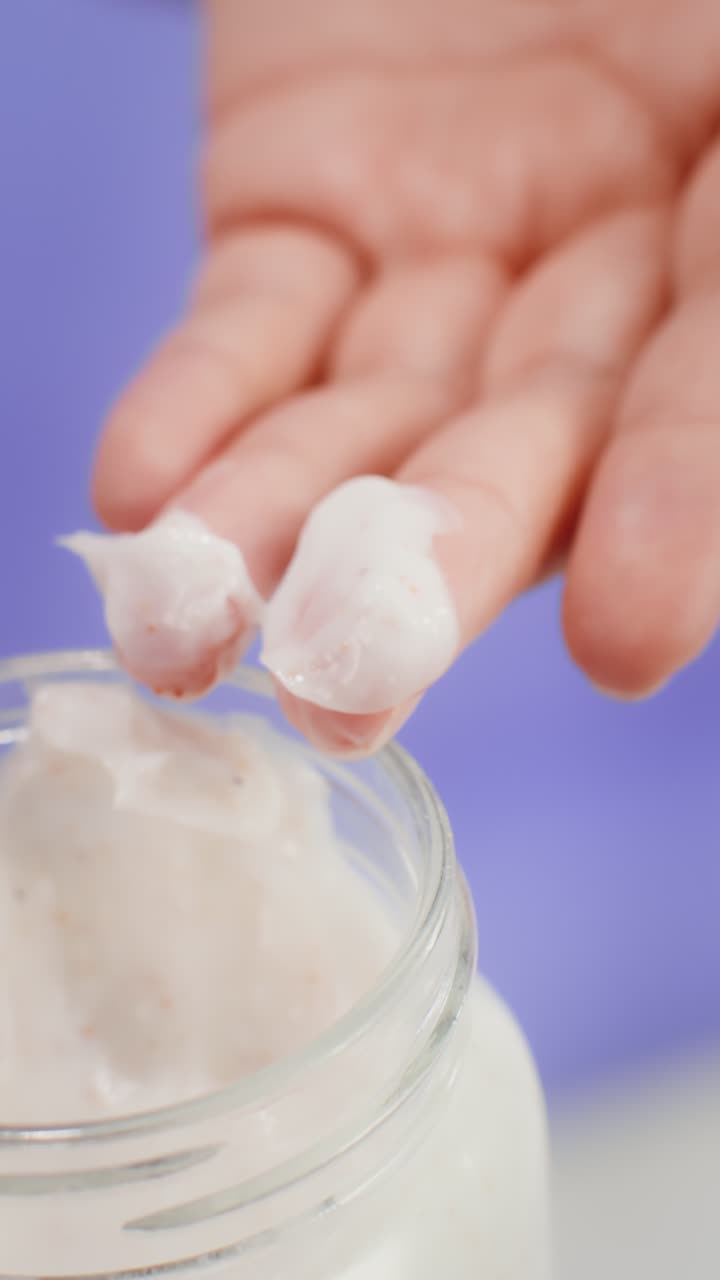 Close-up of a jar of cream with a finger dipping into it