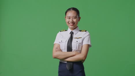 side view of asian woman pilot smiling and crossing her arms to camera while standing in the green screen background studio