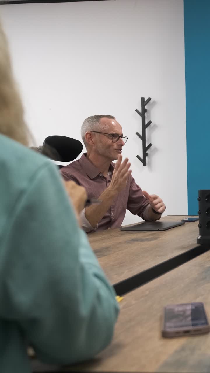 Enthusiastic senior man leading productive office meeting discussion. Vertical footage