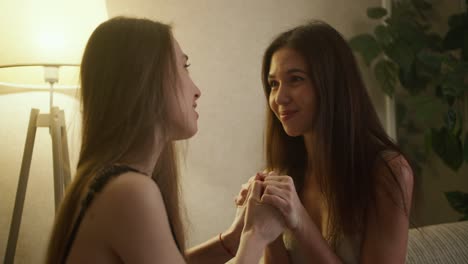 beautiful young lesbian girlfriends sitting on sofa, touching each other and looking with love, slow motion
