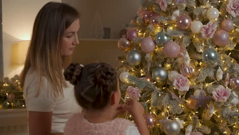 mujer y niña y decoran el árbol de navidad con bolas, luces y adornos