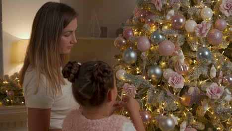 woman and little girl and decorate christmas tree with balls, lights and ornaments