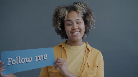 young woman smiling and holding a sign that says 'follow me'