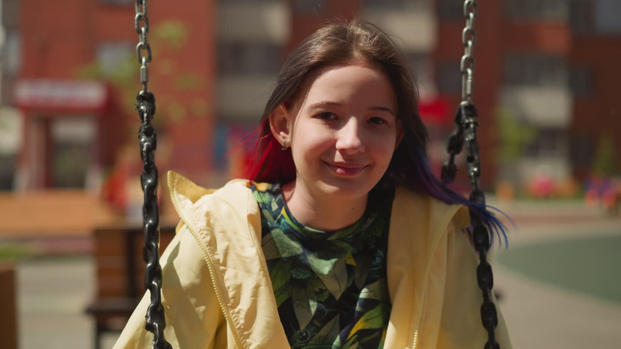 Positive girl with colored strands of hair sits on swing