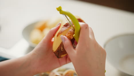close up hand view of person peeling potato with green peeler tool over bowl of scraps, soft blur background adds warmth and domestic feel to detailed cooking preparation scene