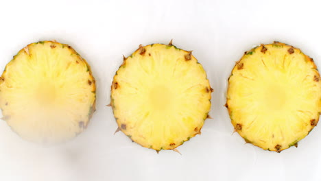 vista superior: 3 rebanadas de piña lavadas con agua sobre un fondo blanco. salpicaduras de agua en cámara lenta.