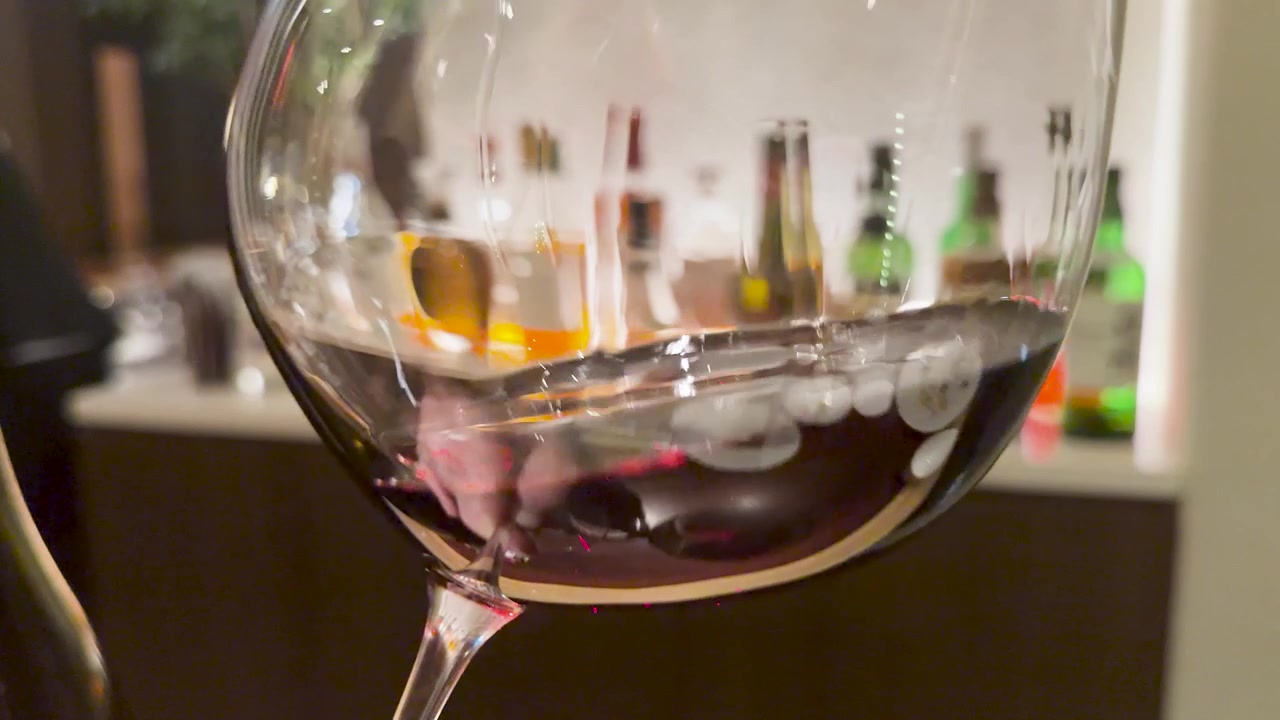 Close-up of red wine swirling inside a glass at a bar with blurred background bottles