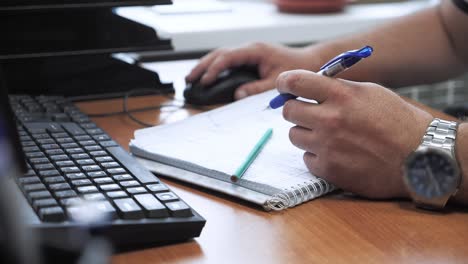 un hombre trabaja en la oficina en la computadora y hace notas en un cuaderno