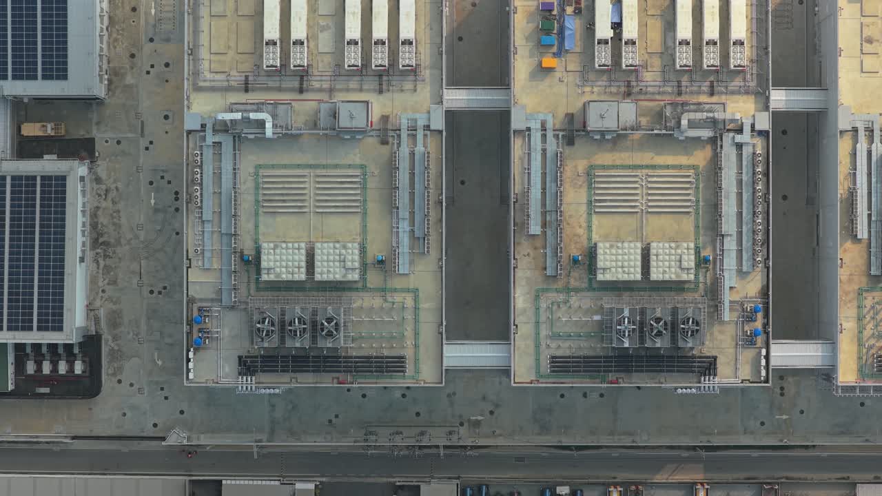 High angle drone perspective flying over an industrial building roof, showcasing hvac units, cooling systems, and solar panels