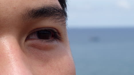 extreme-close-up-of-asiatic-young-black-dark-eye-with-ocean-sea-in-background