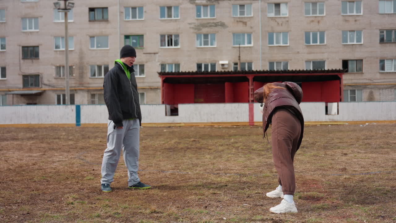 Dos personas jugando al aire libre con alegría, una pareja practicando fútbol en un entorno urbano lleno de energía, disfrutando de una animada y amistosa sesión de fútbol en un bullicioso parque de la ciudad