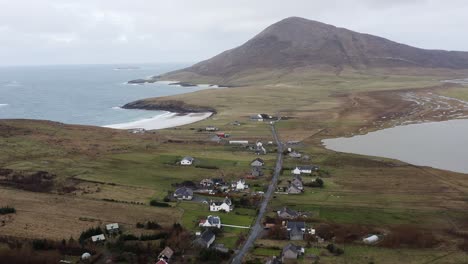 Drone-shot-of-the-village-of-Northton,-featuring-the-surrounding-seascape-and-a-mountain-in-the-background