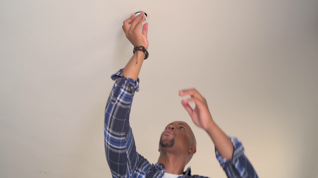 Uomo africano che ispeziona e installa un dispositivo rotondo testando una plafoniera a incasso in soggiorno.