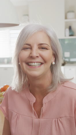 retrato de video vertical de una mujer caucásica senior feliz sonriendo a la cámara en la cocina