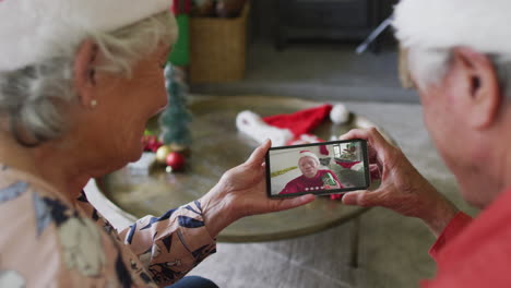 pareja caucásica mayor sonriente usando un teléfono inteligente para una videollamada de navidad con un hombre en la pantalla