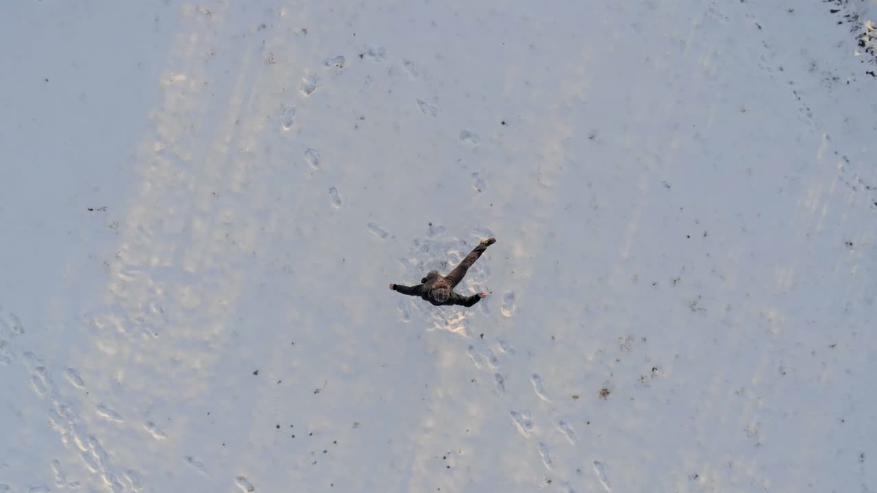 aéreo de arriba hacia abajo del hombre bailando feliz después de la primera nevada en invierno