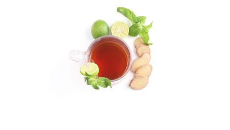 té de limón en una taza de vidrio transparente con hojas de menta de jengibre de limón enteras y en rodajas en un plano superior giratorio de fondo blanco