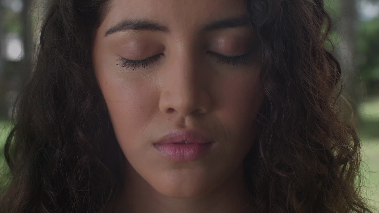 High-quality 4K footage of a serene young woman with curly hair and closed eyes. Shot outdoors in soft, natural light. Ideal for mindfulness, meditation, and wellness advertising