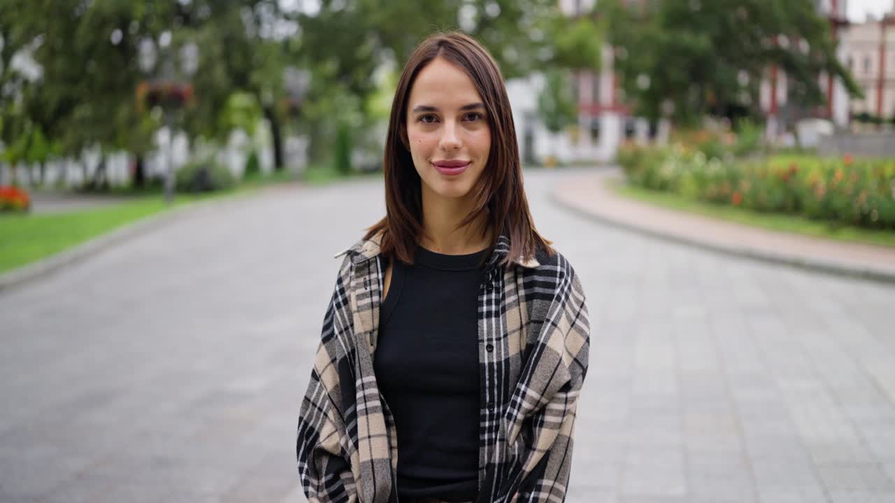 Una giovane donna che sorride e guarda la macchina fotografica mentre è in piedi in un parco