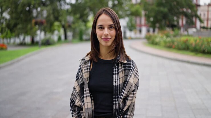 Una giovane donna che sorride e guarda la macchina fotografica mentre è in piedi in un parco