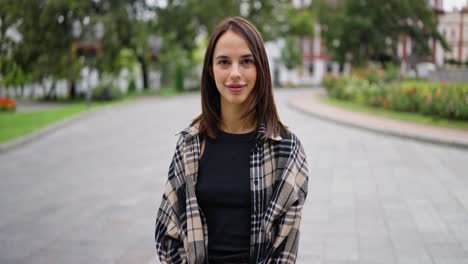 a young woman smiling and looking at the camera while standing in a park.