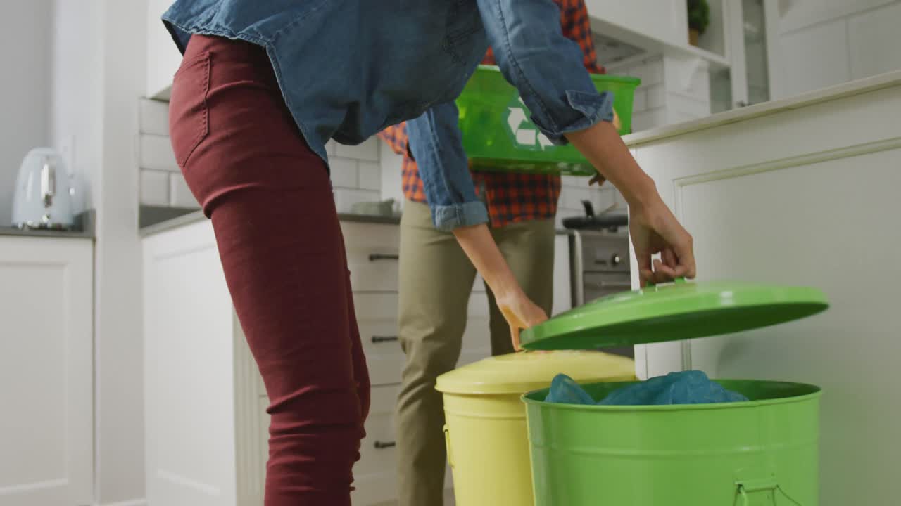 pareja diversa con camisa y chaqueta segregando residuos en la cocina