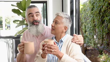 senior couple holding coffee mugs, enjoying time together at home