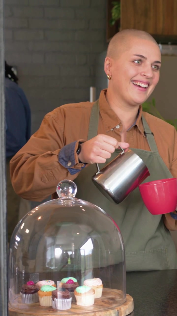 Video verticale: Cliente che chiede un latte macchiato, barista con grembiule versa il latte dalla lattiera in una tazza rossa al bar