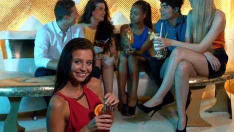 Portrait-of-woman-holding-a-cocktail-while-friends-sitting-behind