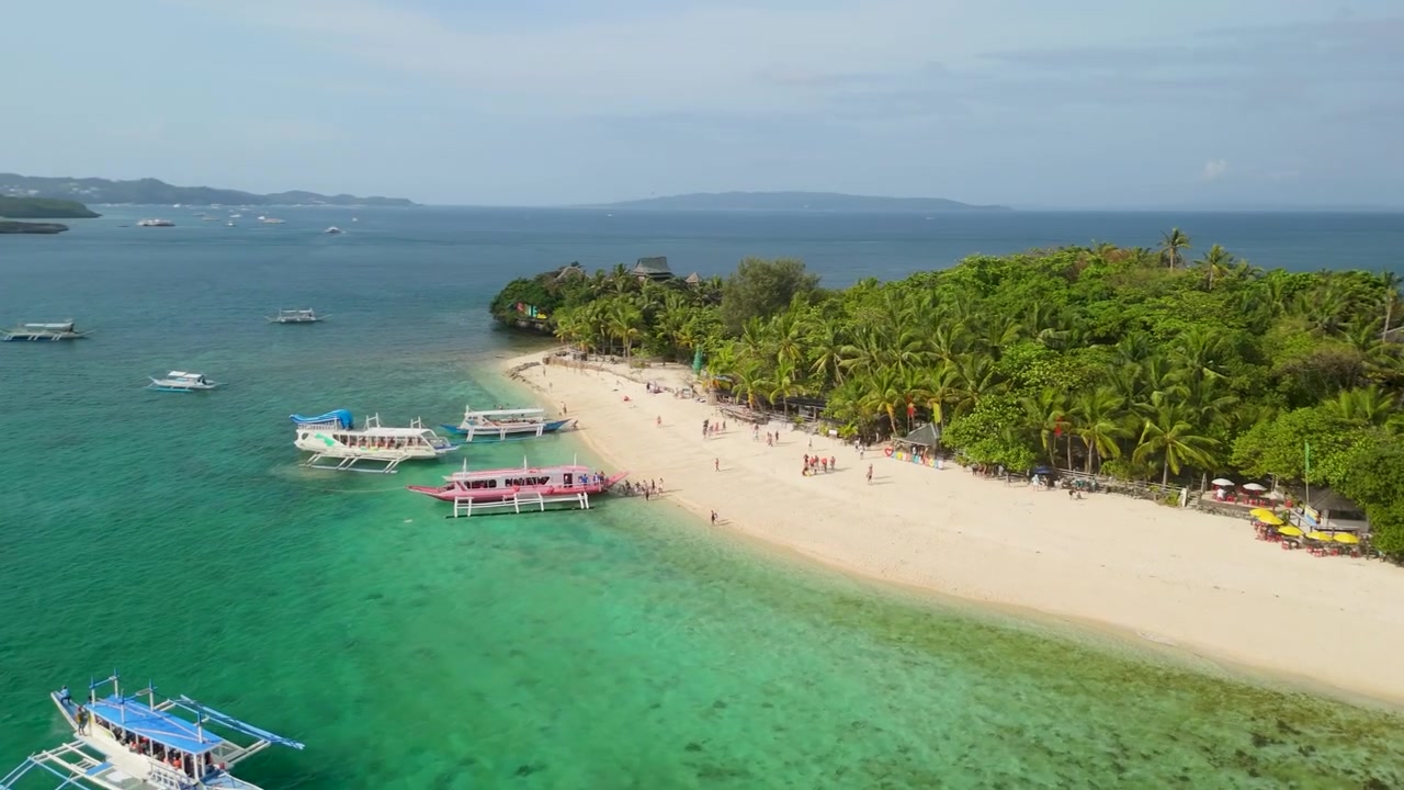 Parallasse aerea che rivela il piccolo resort sull'isola Crystal Cove con spiaggia di sabbia bianca e turisti, barche bangka colorate, acque color smeraldo e una lussureggiante volta tropicale vicino a Boracay, Filippine.