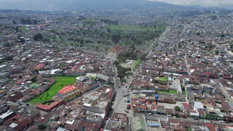 Drone-aerial-footage-of-urban-colonial-traffic-driving-through-streets-of-Central-American-highlands-city-Quetzaltenango,-Xela,-Guatemala-on-a-sunny-day-near-Parque-El-Calvario-and-Cementerio-General