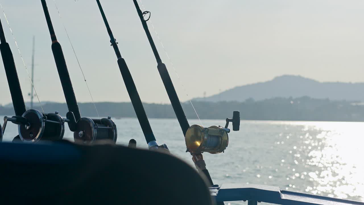 Fishing rods on a boat in Phuket, Thailand, with serene ocean and mountain backdrop. Bright daylight and calm atmosphere