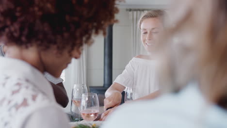 group of young friends sitting around table at home enjoying meal together