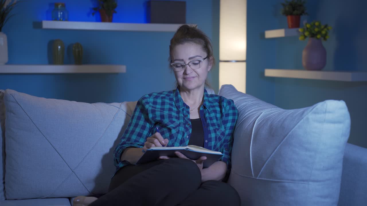Happy woman at home at night keeping a diary. Woman both thinks and writes.