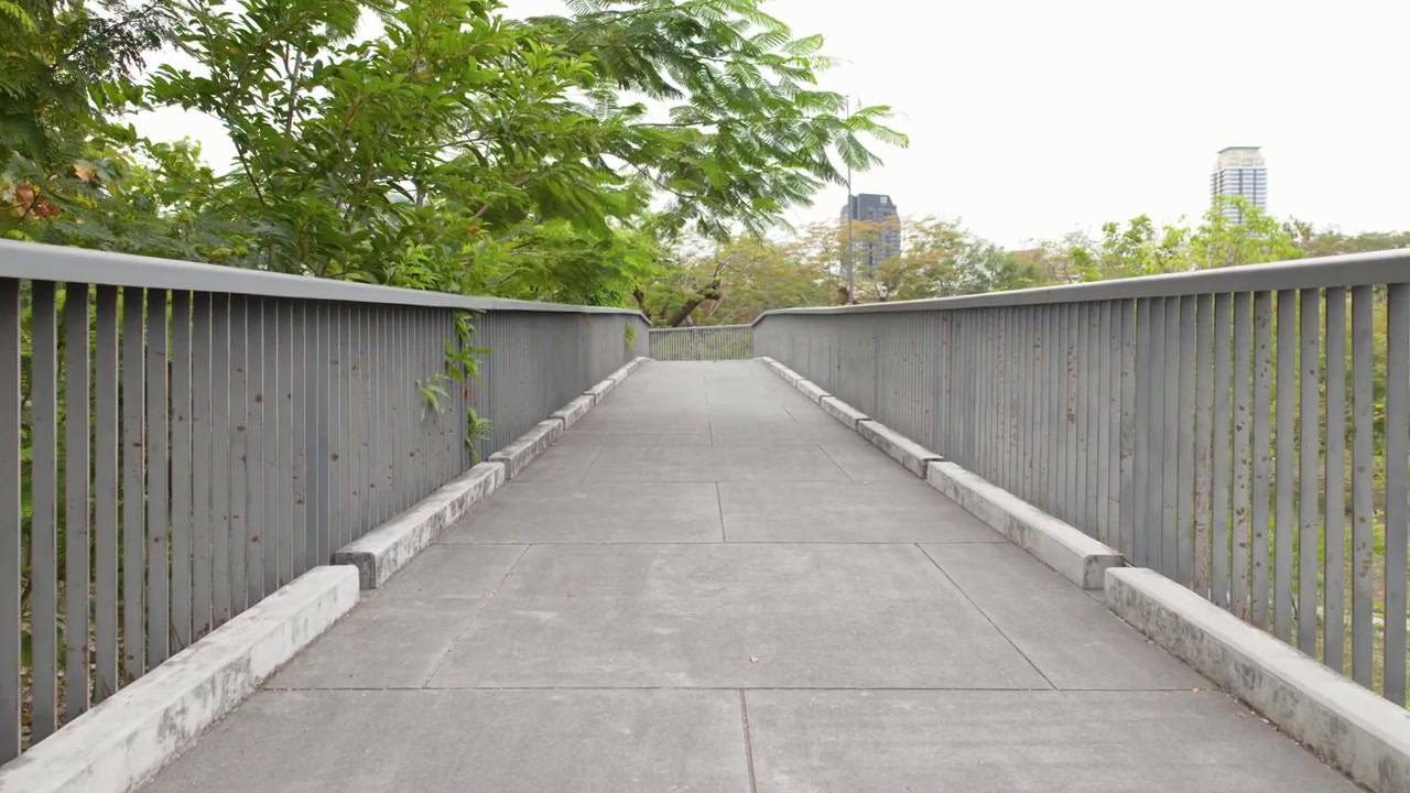 A steady camera moves forward along a modern elevated skywalk surrounded by dense tropical foliage