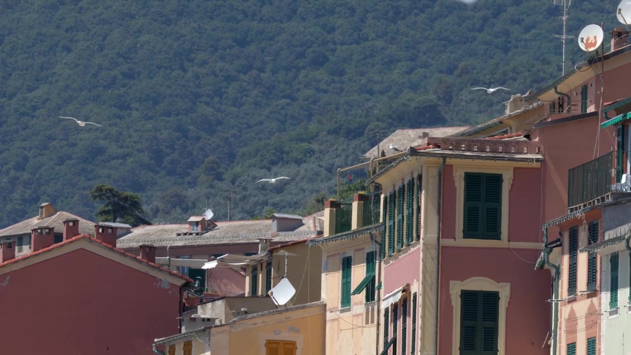 Inquadratura media statica di vivace architettura di un villaggio italiano su uno sfondo di montagne verdi e lussureggianti.