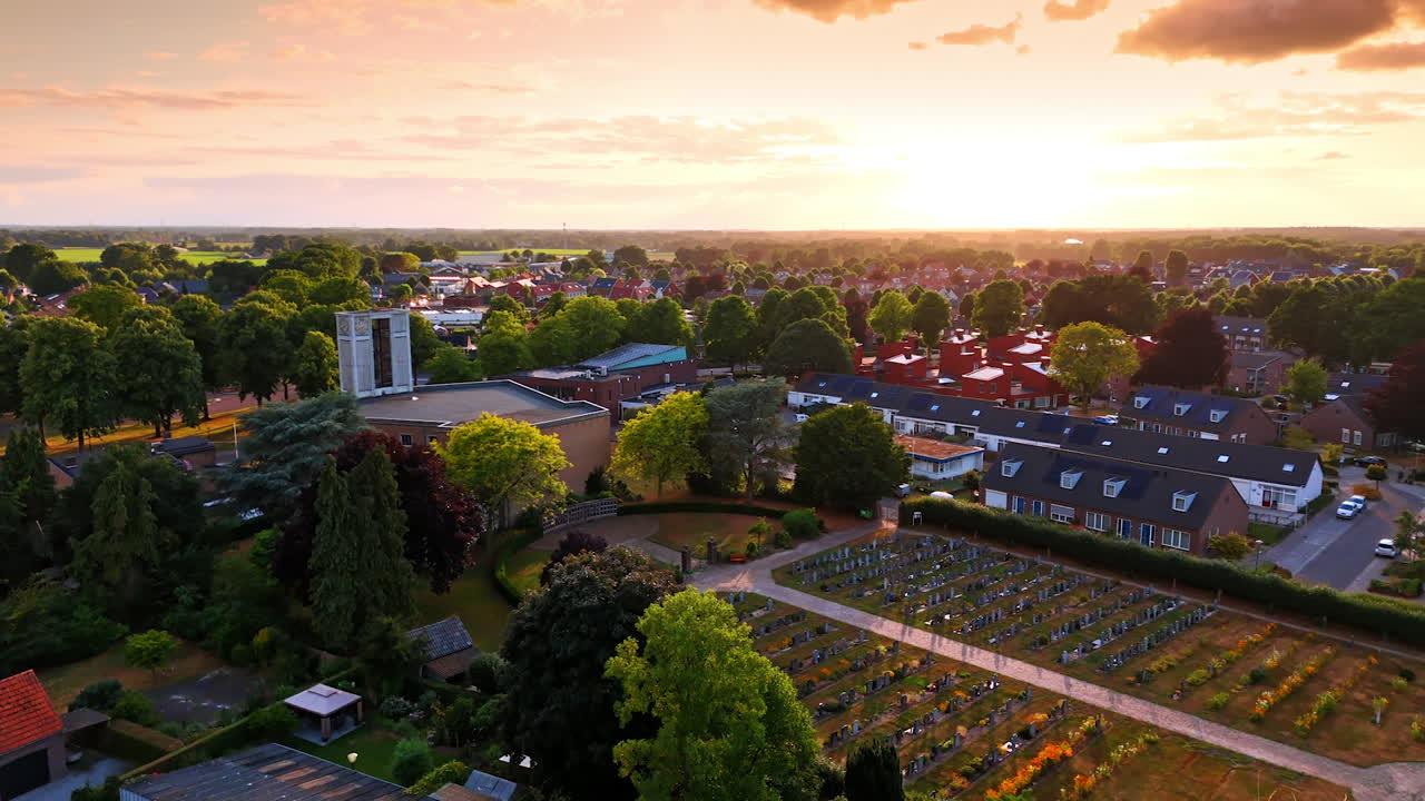 Cemetery at sunset in a quiet town. A serene cemetery sits surrounded by trees, with houses in the distance as the sun sets on a peaceful community