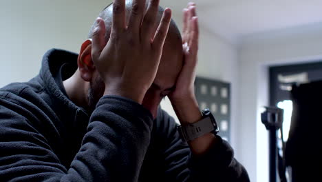 man covering face with hands, showing despair, in dimly lit room, possible headache or stress, , close-up