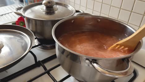 stir tomato soup with a wooden spoon, cooked in a steel pot on a gas stove