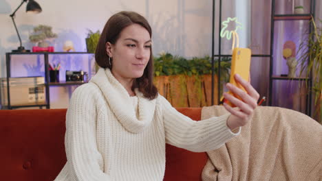 Mujer-Joven-Haciendo-Una-Videollamada-Selfie-En-Línea,-Hablando,-Saludando-Con-La-Mano,-Mirando-A-La-Cámara-En-Casa