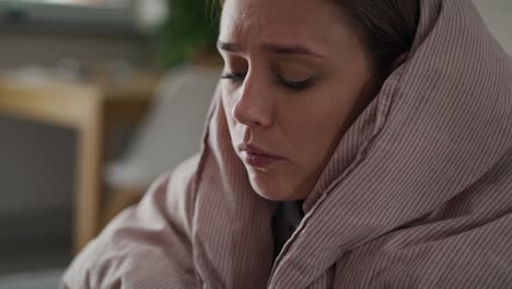 caucasian young woman coughing and sitting under the duvet at home.