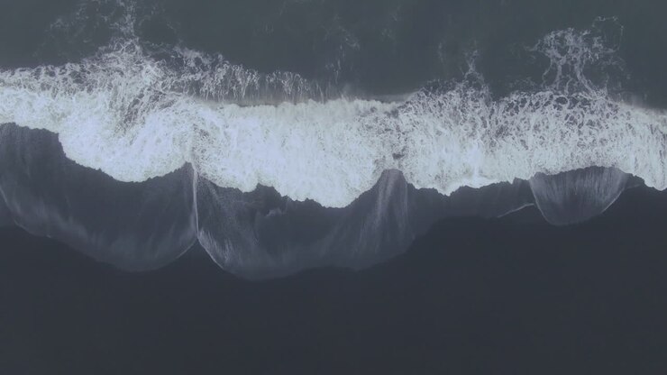Aerial drone straight down waves crashing at Vik Iceland early winter fog at Black Sand Beach