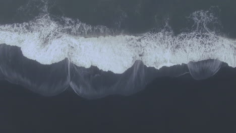 Aerial-drone-straight-down-waves-crashing-at-Vik-Iceland-early-winter-fog-at-Black-Sand-Beach